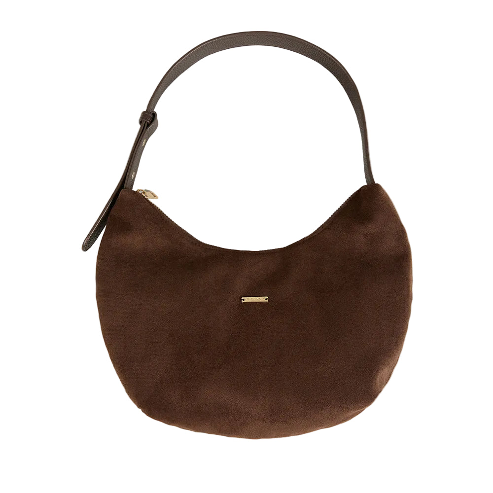 A brown suede crescent-shaped shoulder bag with a dark brown leather strap and a small gold metal accent on the front, set against a solid light gray background.